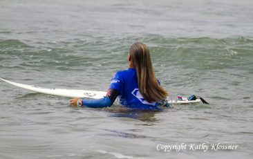 Chelsea Tuach standing by her surfboard in the ocean
