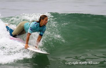 Paige Hareb kneeling on her surfboard on a wave